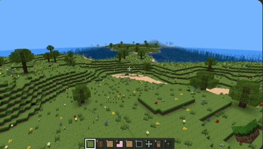 BlockCraftの花が咲く草原と湖を上空から見渡すゲーム画面